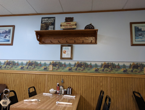 A cozy diner interior with wooden tables, bear-themed decor, and a shelf displaying signs and framed pictures.