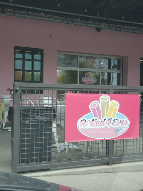 Exterior of Rolled Fever ice cream shop with a pink wall and a sign featuring colorful ice cream rolls.