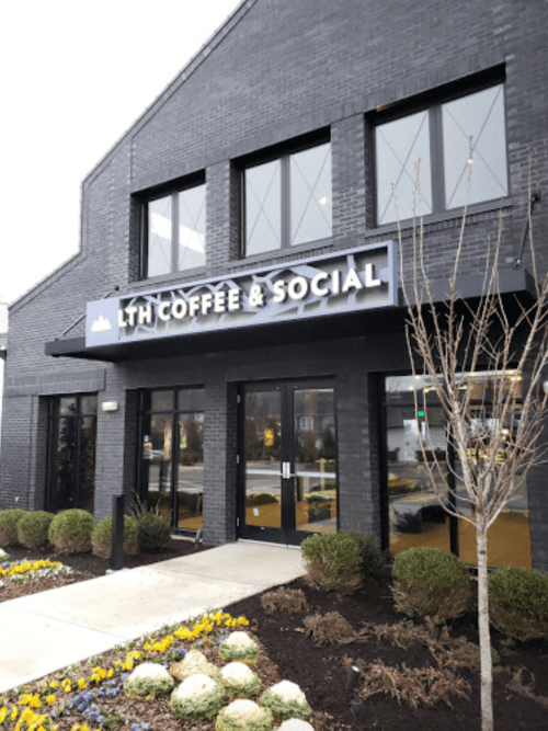 Exterior of LTH Coffee & Social, featuring a modern black building and landscaped flower beds.