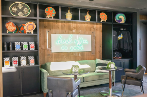 Cozy coffee shop interior with a green couch, tables, and colorful wall decor, featuring a neon sign that reads "drink coffee, do good."
