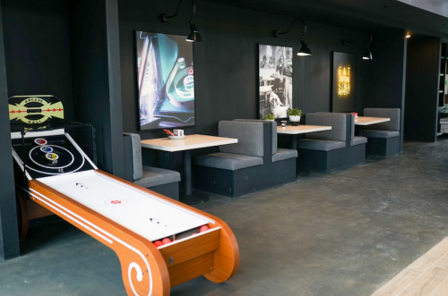 A modern cafe interior featuring a shuffleboard table and cozy booth seating against dark walls.
