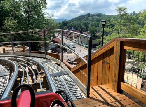 View from a roller coaster track overlooking a scenic landscape with trees and a distant town.