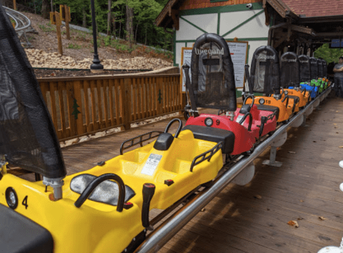 A row of colorful alpine coaster carts lined up on a track at a mountain amusement park.