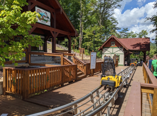 A scenic view of a mountain coaster station with wooden tracks and lush greenery in the background.