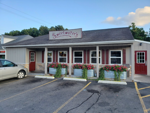 A cozy restaurant exterior with a sign reading "Sweetwater's," featuring flower planters and a welcoming entrance.