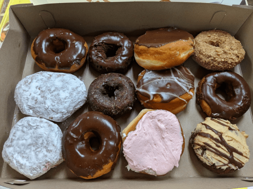 A box of assorted donuts, including chocolate, glazed, powdered, and frosted varieties.