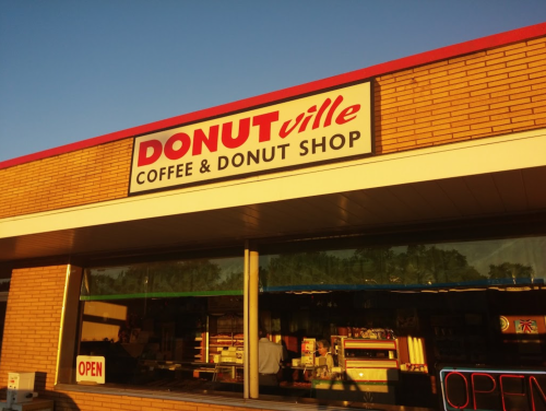 Sign for "DONUTville Coffee & Donut Shop" with an "OPEN" sign visible in the window. Bright blue sky in the background.