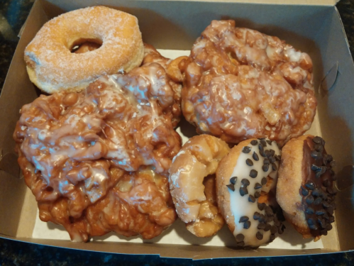 A box of assorted donuts, including glazed apple fritters, a plain donut, and chocolate chip-topped donuts.