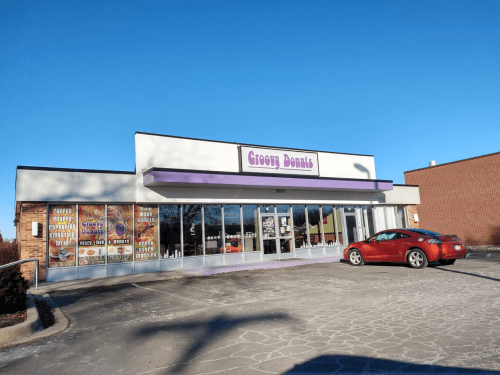 A colorful donut shop named "Groovy Donuts" with large windows and a red car parked outside on a clear day.