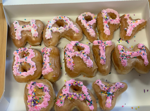 A box of donuts shaped like letters, spelling "HAPPY BIRTHDAY" with pink icing and colorful sprinkles.