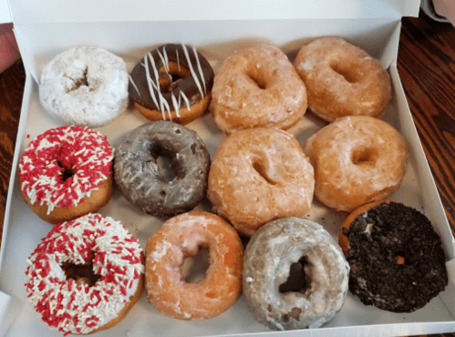 A box of assorted donuts, featuring glazed, chocolate, and sprinkled varieties in various colors and toppings.