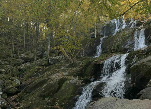 A serene waterfall cascading over rocky terrain, surrounded by autumn foliage and trees.