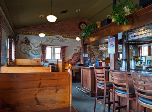 Cozy restaurant interior with wooden booths, a bar area, and colorful murals on the walls. Warm lighting enhances the ambiance.