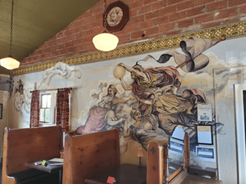 A mural depicting a dramatic scene with figures and clouds, set in a cozy restaurant interior with wooden booths.