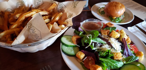 A plate of salad with croutons and cucumbers, accompanied by a basket of fries and a small burger on the side.