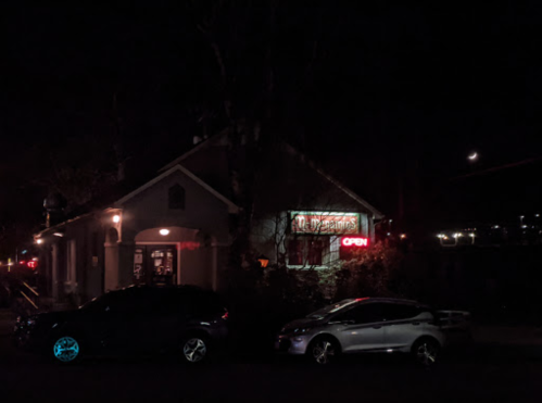 A dimly lit building at night with an "Open" sign and parked cars in front.