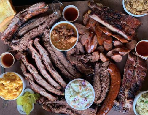 A spread of various meats including ribs, sausage, and brisket, accompanied by sides of coleslaw, baked beans, and macaroni.