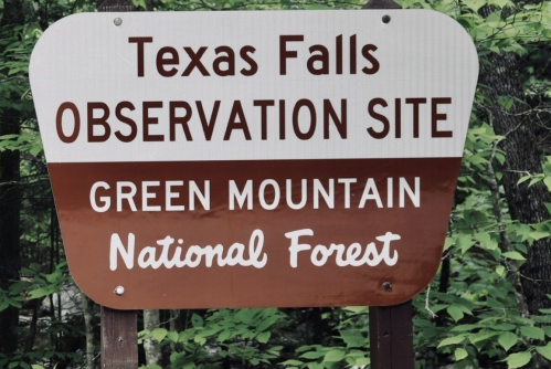 Sign for Texas Falls Observation Site in Green Mountain National Forest, surrounded by greenery.