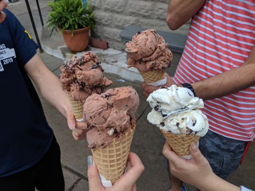 Five ice cream cones with chocolate and vanilla flavors held by people, set against a stone wall.