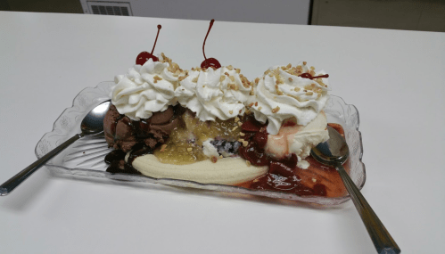 A banana split topped with chocolate and vanilla ice cream, whipped cream, nuts, and cherries in a glass dish.