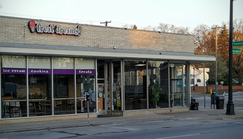 Exterior of "treat dreams!" ice cream shop, featuring large windows and a sign, with a street view in the background.