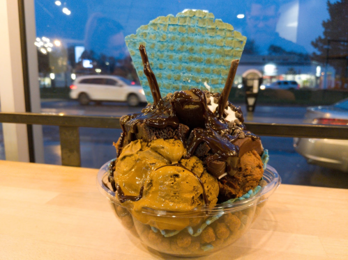 A colorful ice cream sundae in a clear bowl, topped with chocolate sauce, cookies, and a blue waffle cone.
