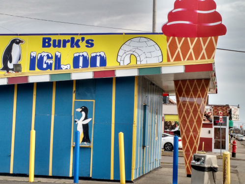 Colorful ice cream shop exterior featuring a large ice cream cone sign and a penguin illustration.