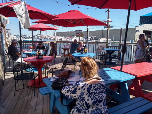 Outdoor dining area with colorful tables and umbrellas, overlooking a marina with boats in the background.