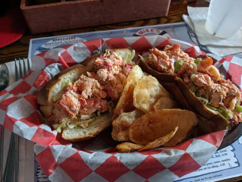 Two lobster rolls with lettuce in a basket, accompanied by a side of potato chips.