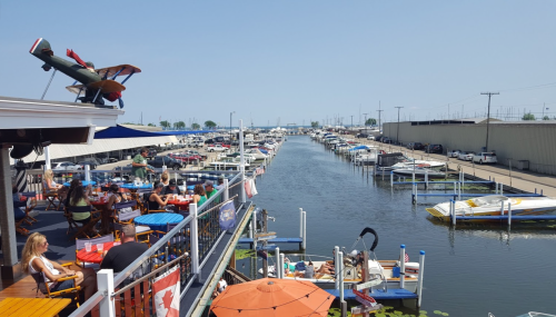 A view from a restaurant deck overlooking a marina filled with boats and people enjoying the sunny day.
