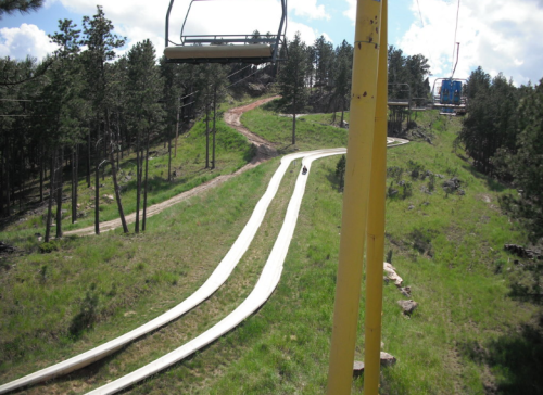 A winding slide through a green landscape, with a ski lift in the foreground and trees in the background.