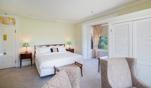 Bright, airy bedroom with a large bed, two lamps, and a cozy seating area by a window. Soft pastel decor.