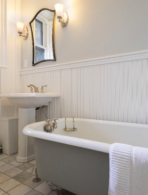 A bright bathroom featuring a vintage clawfoot tub, a pedestal sink, and elegant wall sconces.