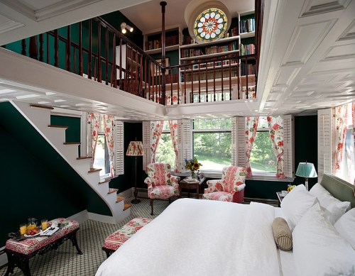 Cozy bedroom with a loft, floral decor, large windows, and a colorful stained glass feature.