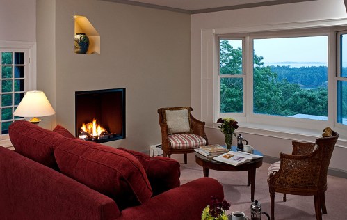 Cozy living room with a red sofa, two chairs, a coffee table, and a view of nature through large windows.