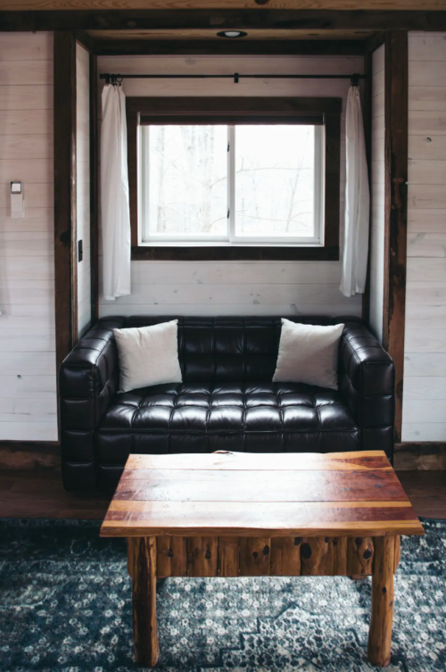 A cozy living space featuring a black leather couch with two pillows and a wooden coffee table, near a window.