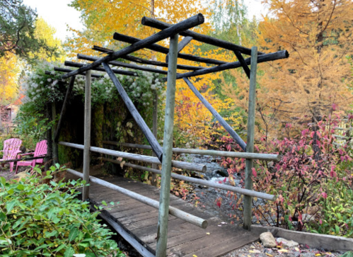 A wooden bridge with a simple frame, surrounded by vibrant autumn foliage and a small stream.