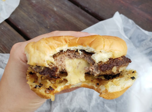 A hand holding a half-eaten cheeseburger with melted cheese and caramelized onions on a soft bun.