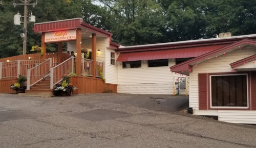 A cozy restaurant with a red roof and wooden steps, surrounded by greenery and festive lights.