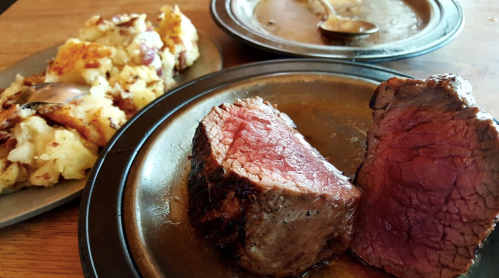 A plate with two slices of juicy roast beef and a side of mashed potatoes, with gravy in a separate dish.