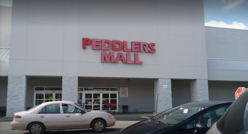 Exterior of Peddlers Mall with a large sign, featuring parked cars in front and a clear blue sky above.