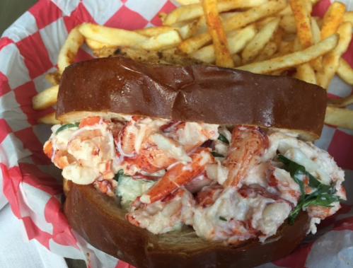 A lobster roll with creamy filling on a brioche bun, served with a side of golden French fries.