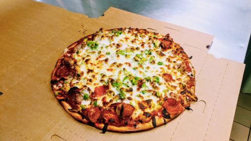 A freshly baked pizza with pepperoni, green peppers, and melted cheese on a cardboard box.
