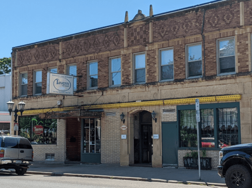 A brick building with a sign reading "Tavern," featuring large windows and a welcoming entrance.