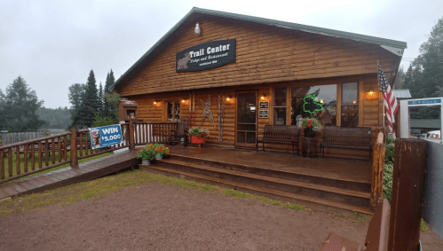 A rustic wooden building with a sign reading "Trail Center," surrounded by flower pots and a "Win $5,000" banner.