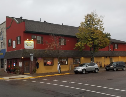 A red and yellow building with an "Open" sign, parked cars, and trees on a cloudy day.