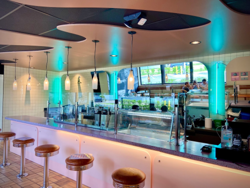 A modern café interior with a sleek counter, pendant lights, and a view of customers enjoying their meals.