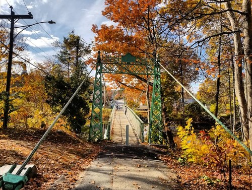 A green suspension bridge surrounded by colorful autumn foliage and a clear blue sky.