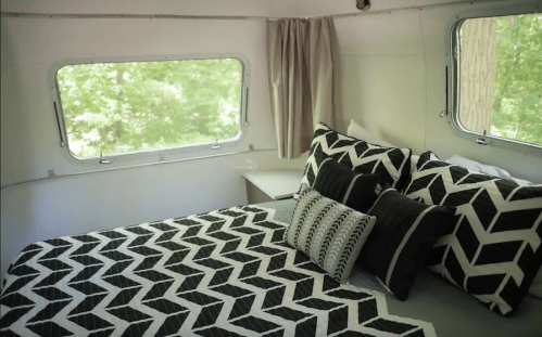 Cozy bedroom with a patterned black and white bedspread and pillows, featuring large windows with a view of greenery.