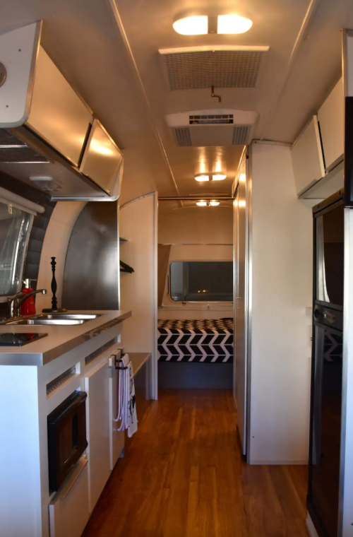 Interior of a modern Airstream trailer featuring a kitchen, dining area, and a bedroom with a patterned bedspread.